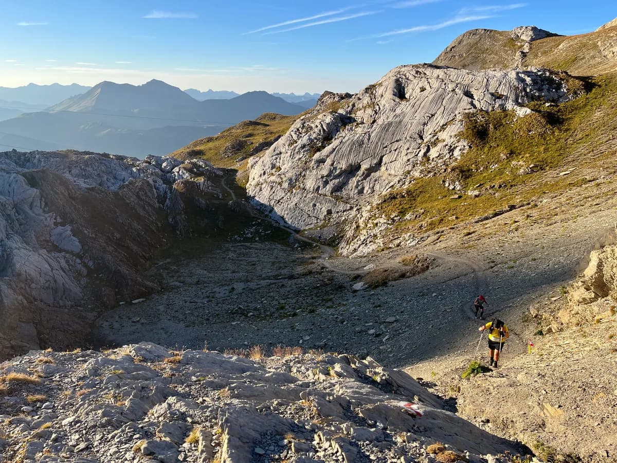 Two runners descending a rocky alpine traverse at golden hour